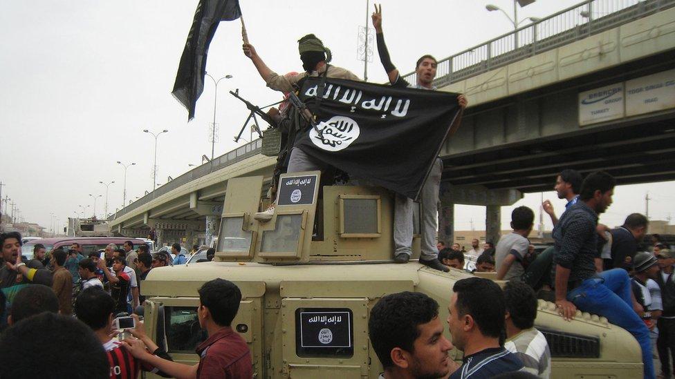 Islamic State militants hold up the group's banner as they patrol in a commandeered Iraqi military vehicle in Falluja, Iraq (30 March 2014)