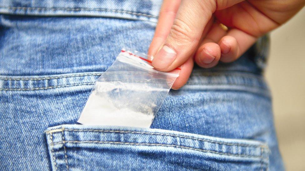 Young person slips a bag of drugs into his back pocket