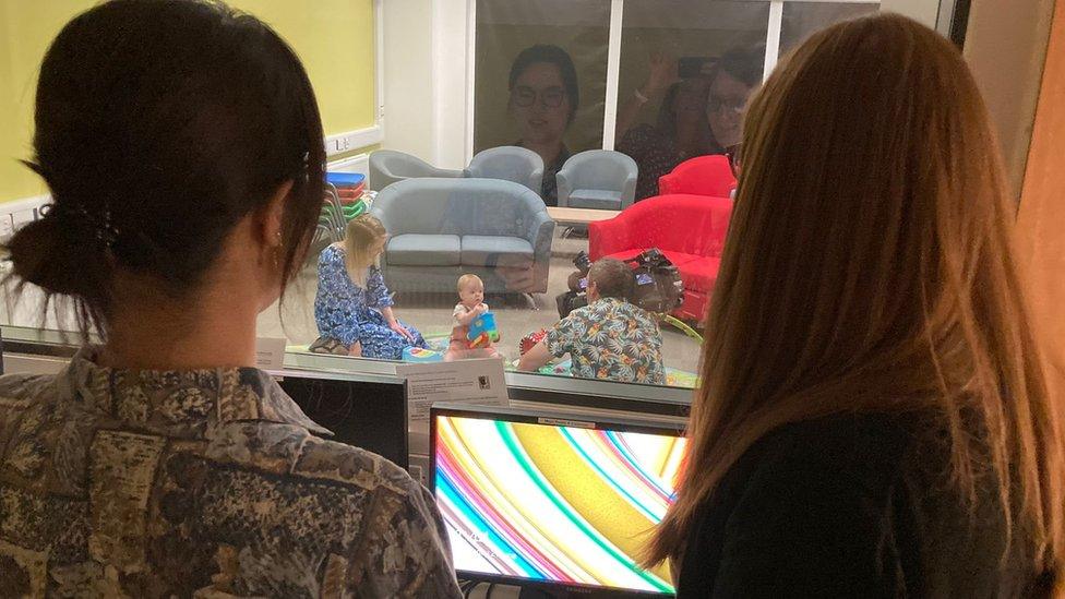 Baby plays with toys while watched by scientists through a screen