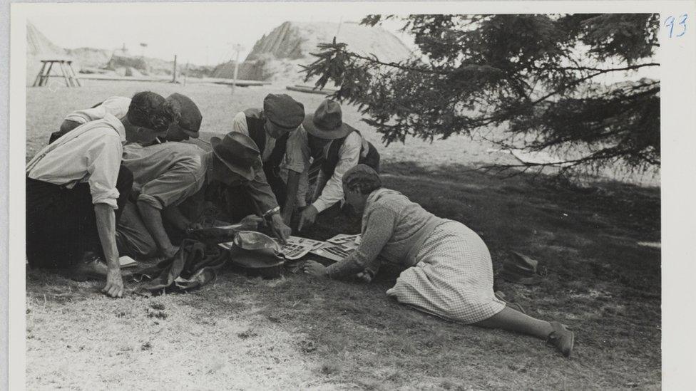 Mercie Lack showing members of the excavation team a selection of contact prints, with the excavation in the background