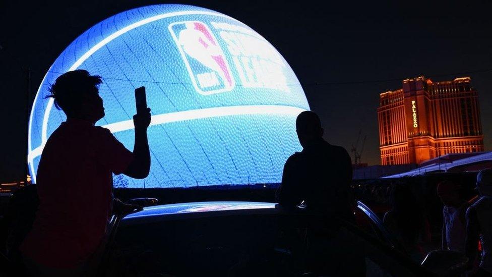 Man photographing sphere lit like a basket ball in Las Vegas.