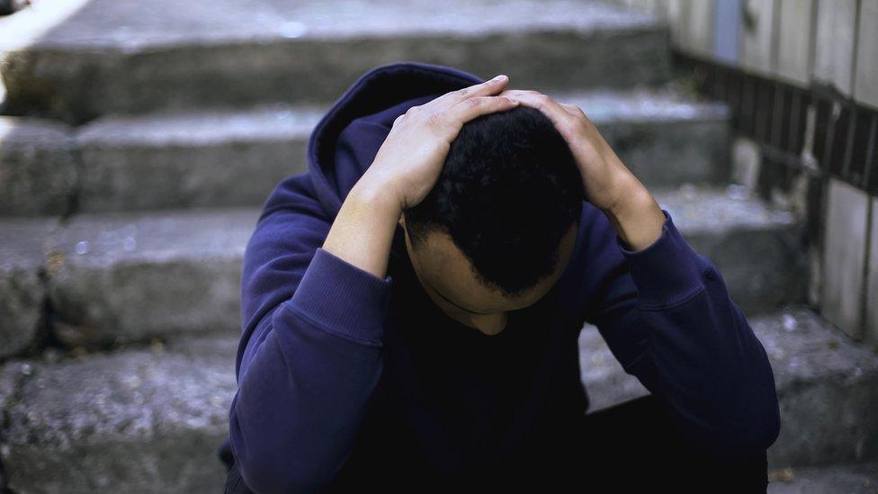 Teenage boy sat on stairs with hands on his head