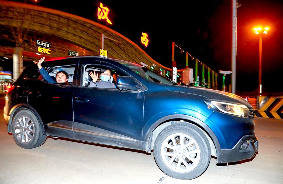 Passengers wave from a car as it passes a toll station