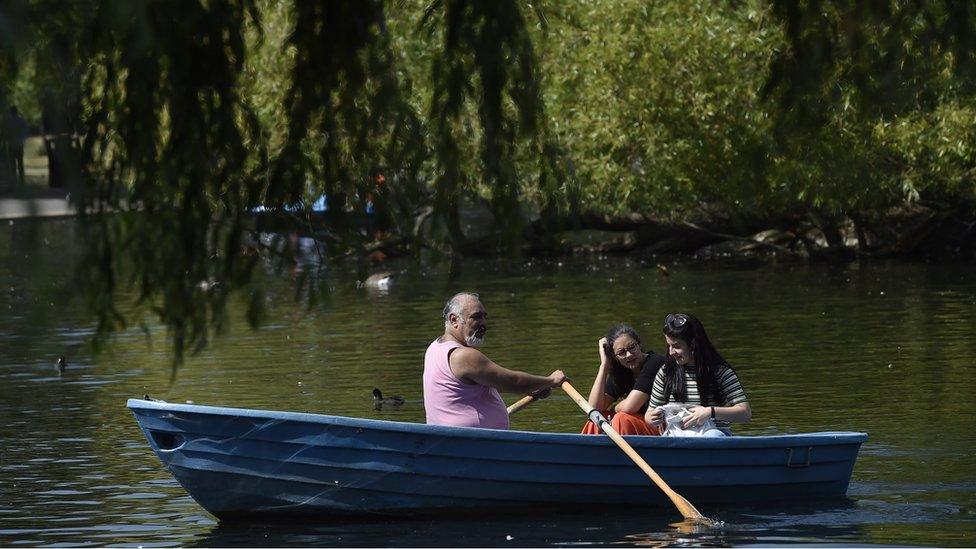 A man and two women in a rowing boat on a lake/pond