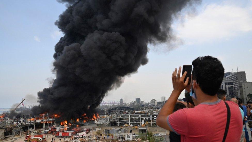 People take pictures as thick smoke billows from a fire at the Port of Beirut, Lebanon, 10 September 2020.