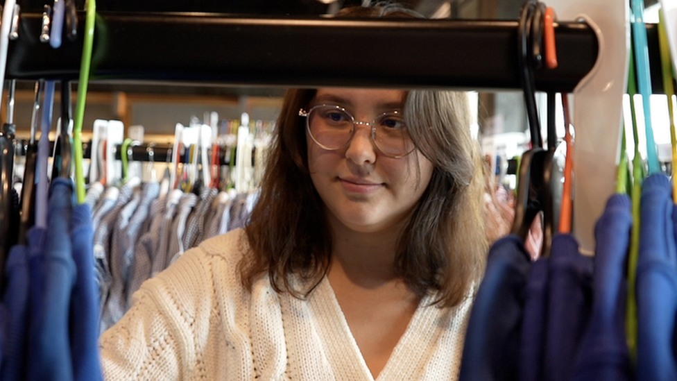 A woman browsing through hangers at the uniform exchange.