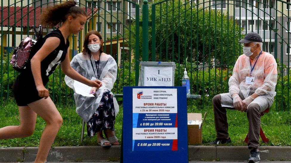 A girl skates her board past members of a local electoral commission wearing face masks in St Petersburg