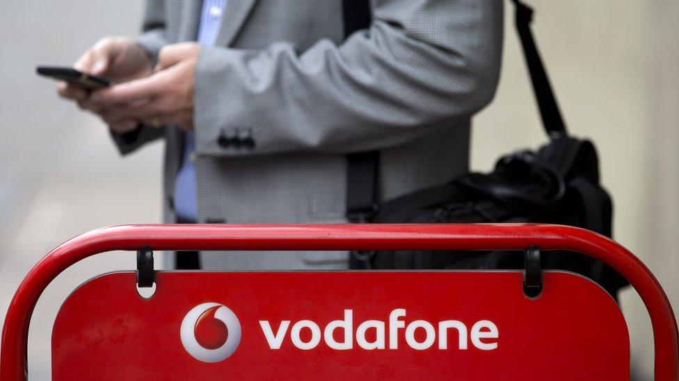 man using phone by Vodafone sign