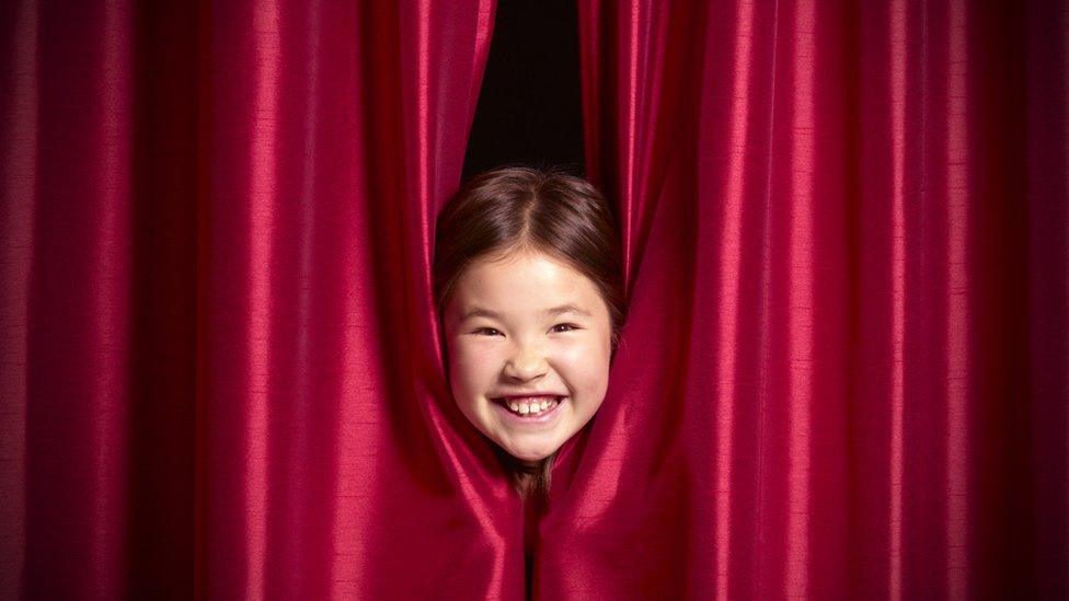 girl smiling behind some curtains