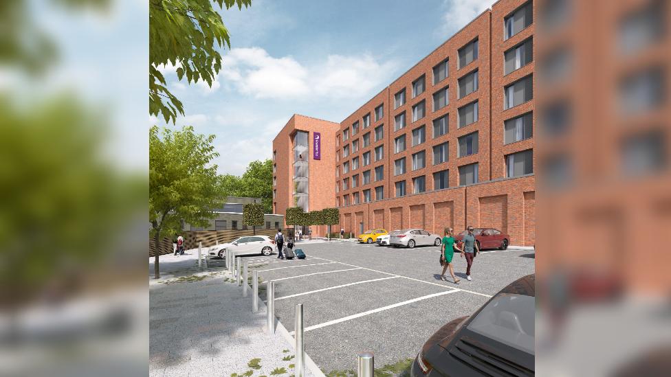 A CGI rendering of what the back of the proposed renewable Premier Inn will look like. It is a large brick building with lots of windows and a car park with trees.