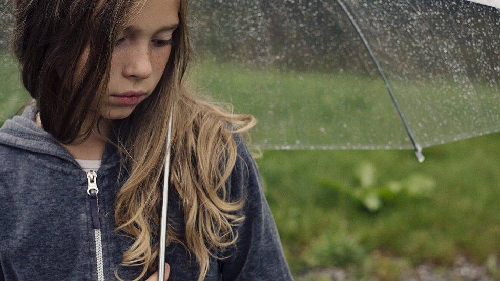 A girls standing under an umbrella in the rain