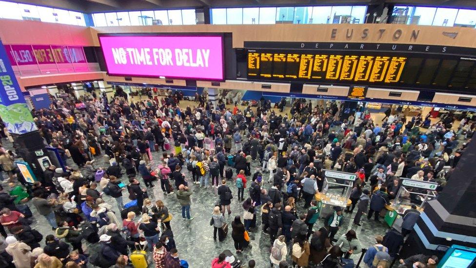 People waiting at Euston under a COP26 sign which says "No time for delay"