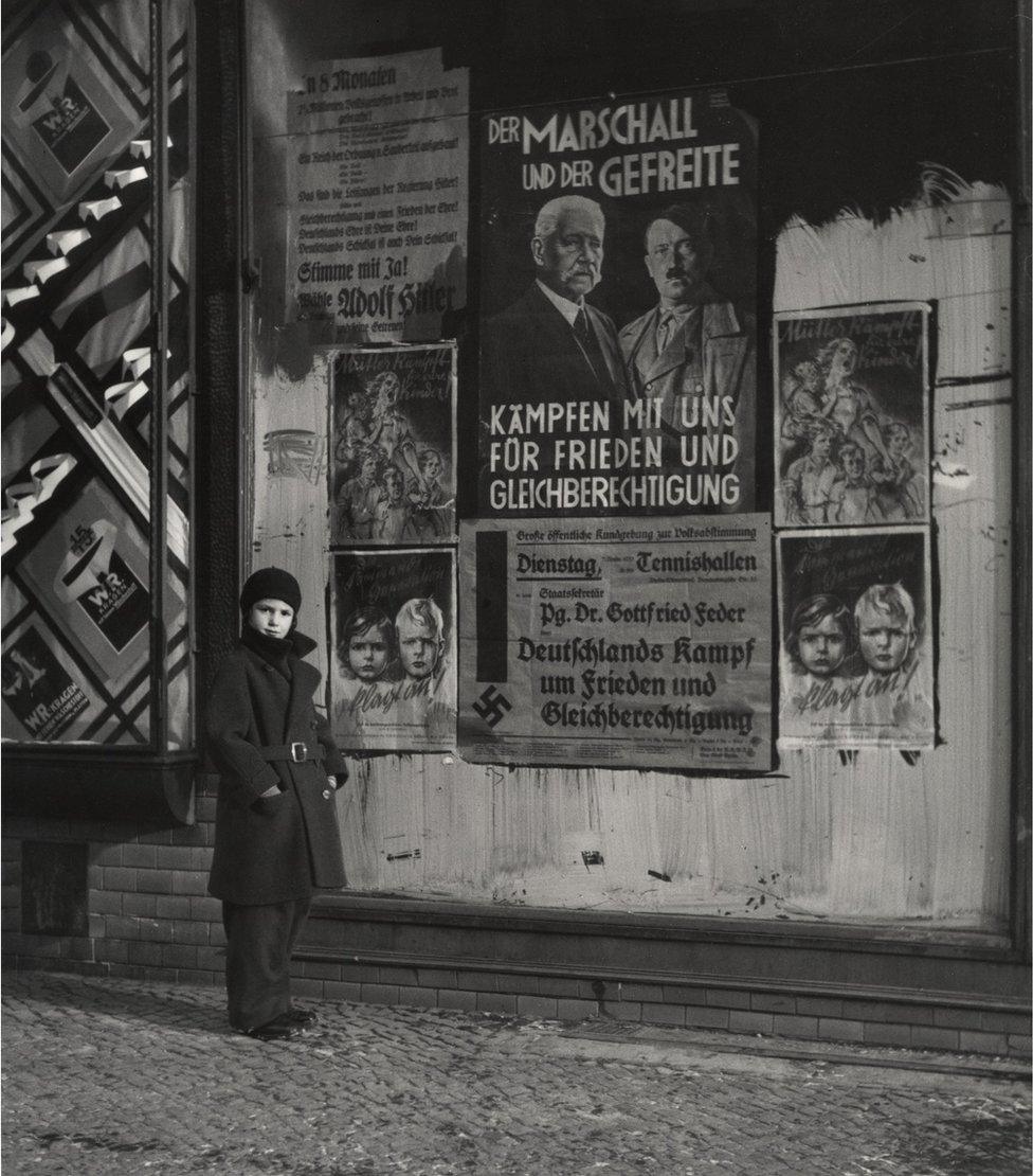 Vishniac's daughter Mara posing in front of an election poster for Hindenburg and Hitler that reads "The Marshal and the Corporal: Fight with Us for Peace and Equal Rights". Wilmersdorf, Berlin, 1933.