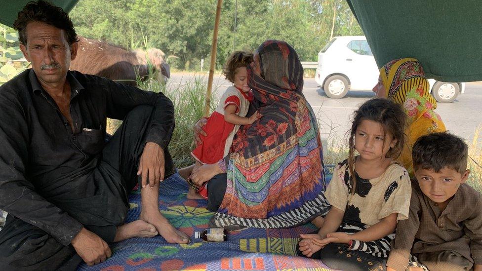 Rozina and her family of young children sit on a rug in the tent they've evacuated to on the side of the road