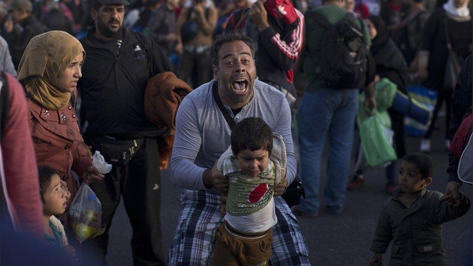 A man holds his child as he tries to talk to Hungarian police officers in Roszke on 7 September 2015