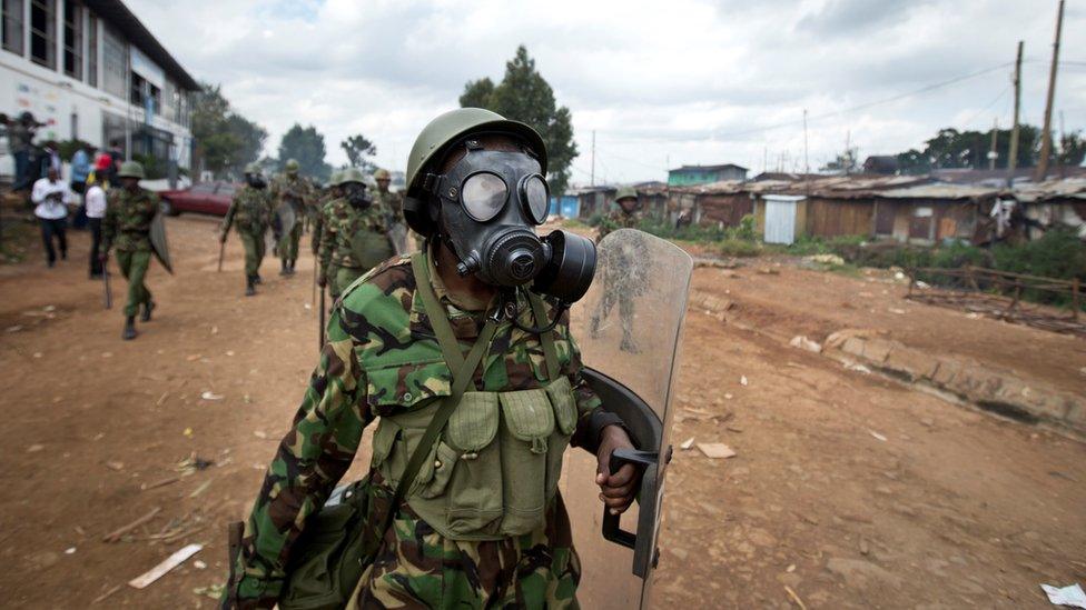 A Kenyan policeman wearing a gas mask chases protesters throwing rocks, in the Kibera slum of Nairobi