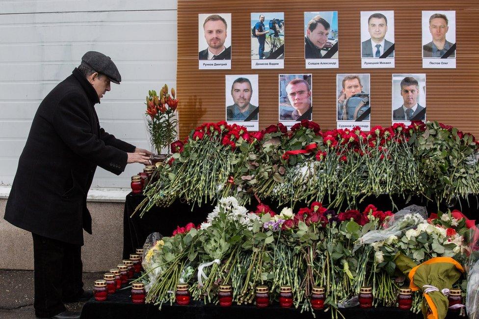 A man places flowers before portraits of Russian TV journalists who were aboard the crashed Tu-154 Russian military plane, at a small memorial outside the Ostankino television centre in Moscow, Russia, 26 December