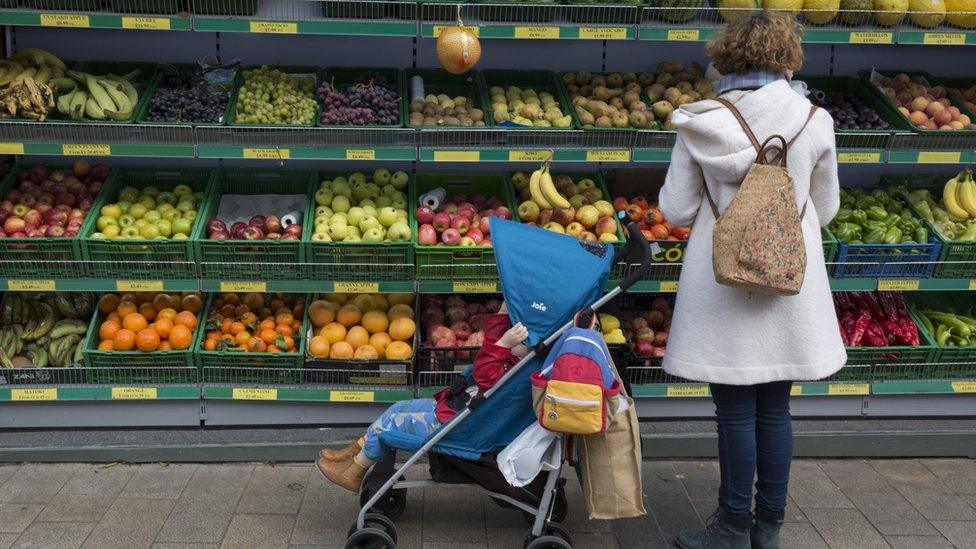 A woman and a child with a pram in front of shelves of fruit and vegetables