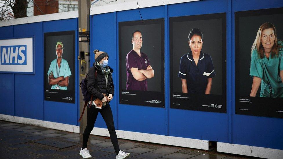 A person walks past images of National Health Service (NHS) workers