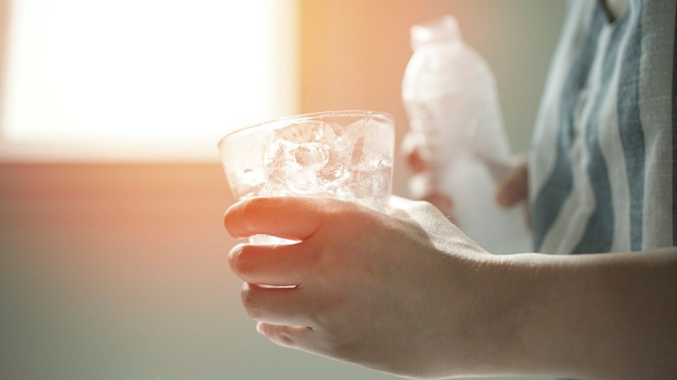 Anonymous hands holding a glass and bottle of water