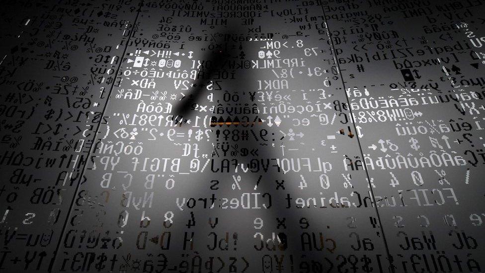 A silhouette of a man walking behind a glass wall with machine coding symbols at the headquarters of Internet security giant Kaspersky in Moscow