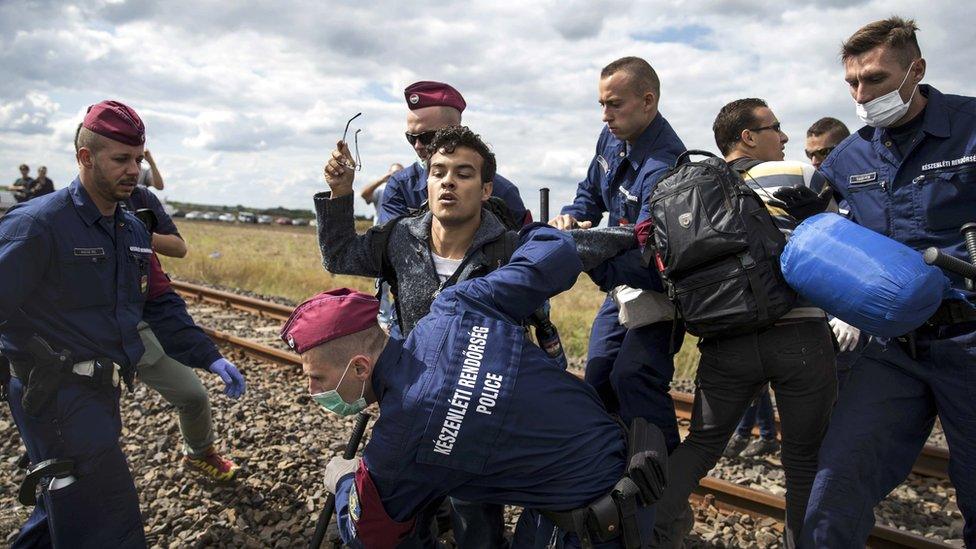 Hungarian policemen attempt to stop a migrant as he tries to escape a collection point in Roszke village, Hungary, on 8 September 2015