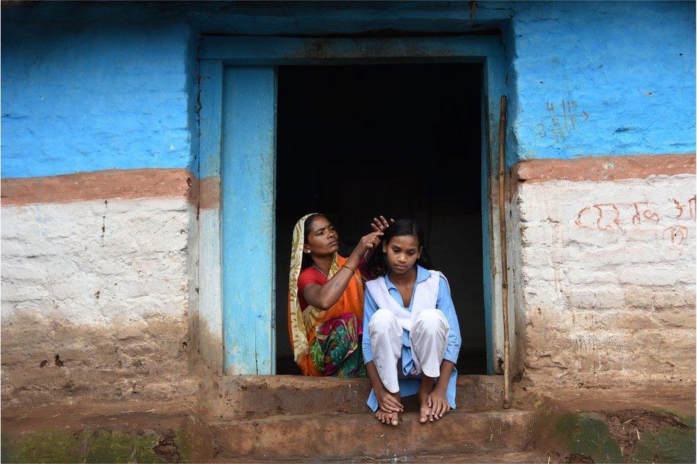 A girl gets her hair combed by her aunt as she gets ready for school.