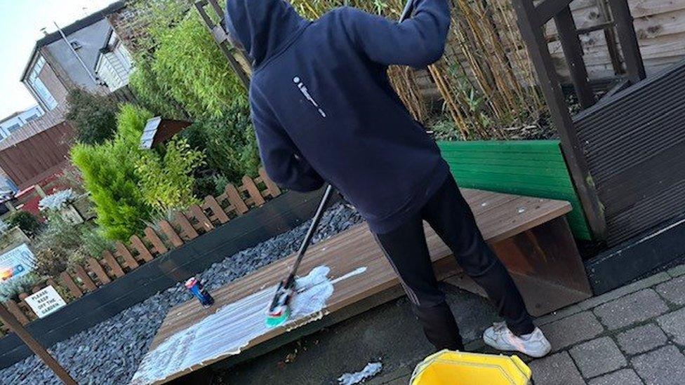 Teenager in a hoody uses mop and bucket to clean mess