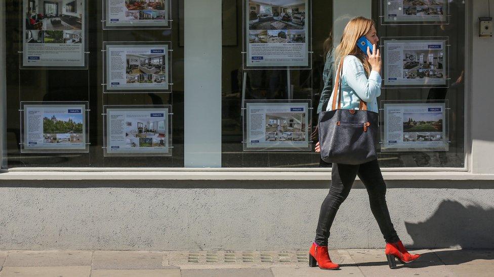 woman walks past estate agents