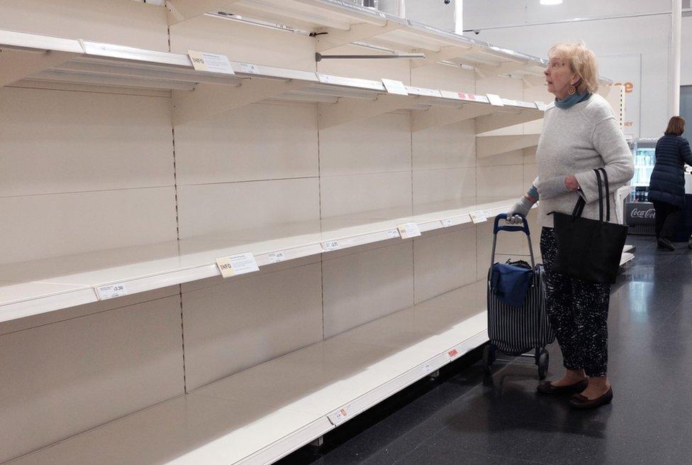 A woman looks at empty shelves in a Sainsbury's store in London, 18 March 2020.