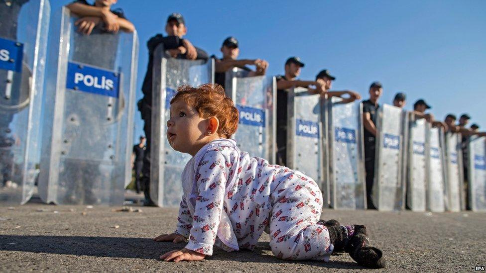 A Syrian refugee baby plays in front of riot police at the Istanbul-Edirne highway as they wait for permission to pass Turkish Greek border to reach Germany in Edirne, Turkey 19 September 2015