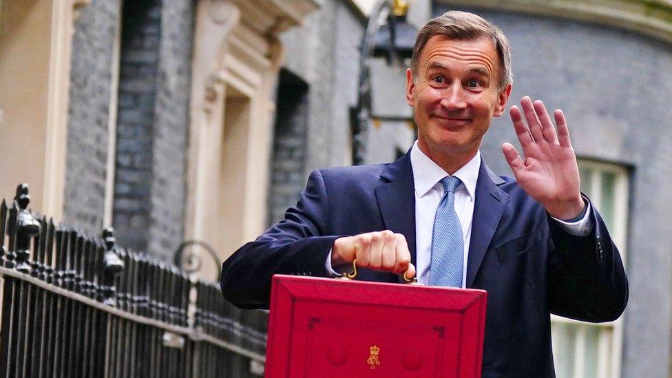 Chancellor Jeremy Hunt waving and holding a red government box.