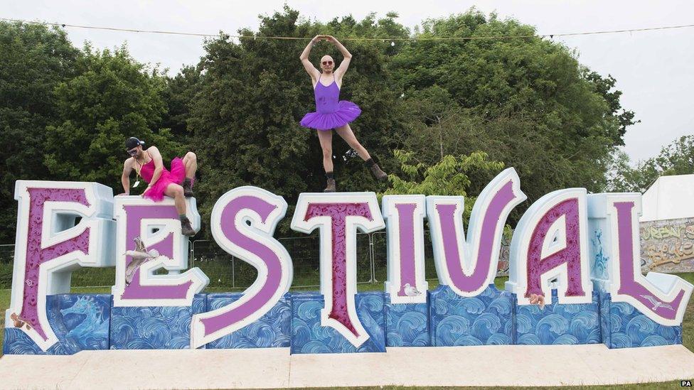 Festival goers in fancy dress on a giant festival sign at the Isle of Wight Festival