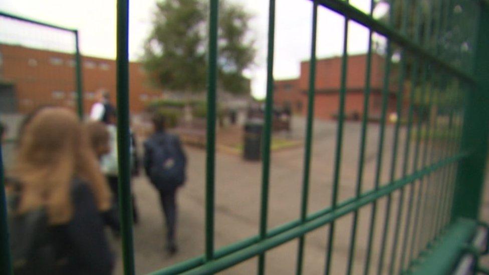 Children walking into a secondary school behind a gate