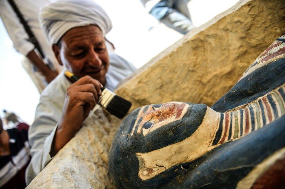 A man brushes off dust from a sarcophagus, part of a new discovery near the Bent Pyramid, about 40km (25 miles) south of Cairo, on 13 July 2019.