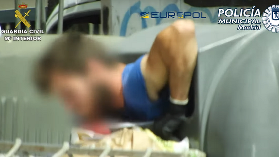 A man's head pokes out of a recycling bin used for waste cardboard and paper