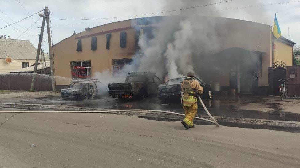 A photo showing a firefighter using a hose to tackle smoke billowing from a building