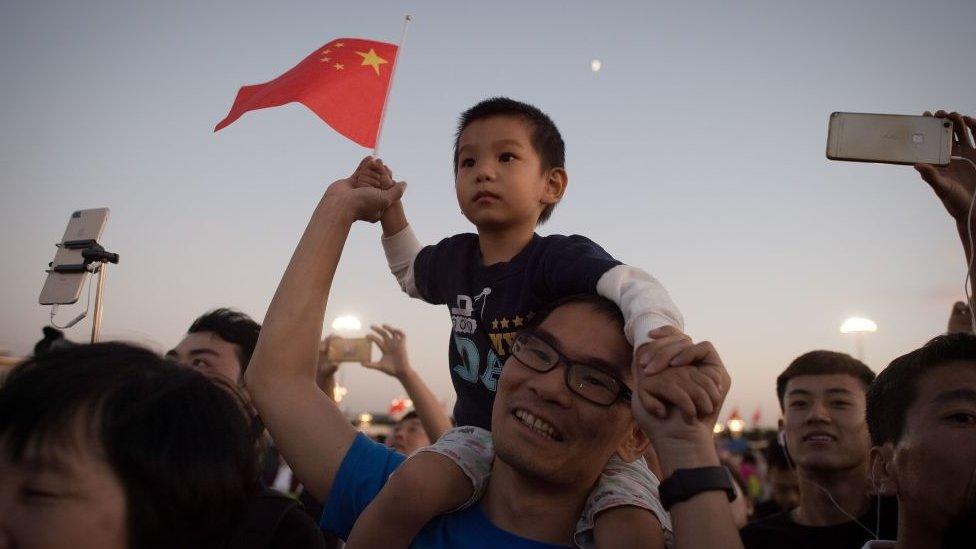 A man carries his son on his shoulders to see the lower of the flag on Tiananmen square in Beijing on September 28, 2017.