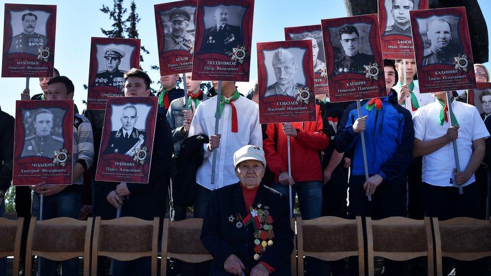 A veteran sits as children hold images of soldiers that fought in the war