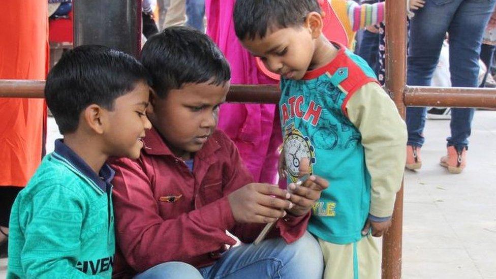 Indian children in Delhi watch something on a mobile phone.