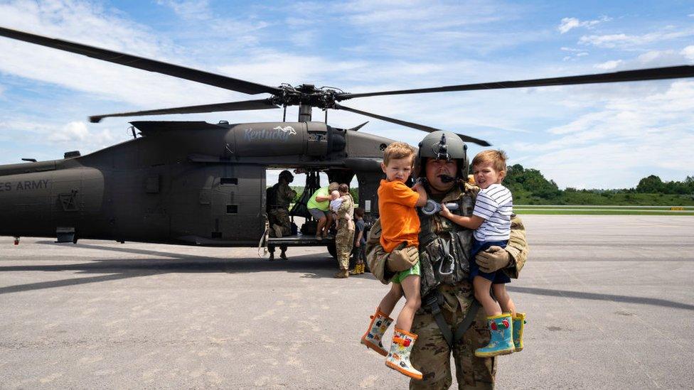 Image shows a National Guardsman carrying two children