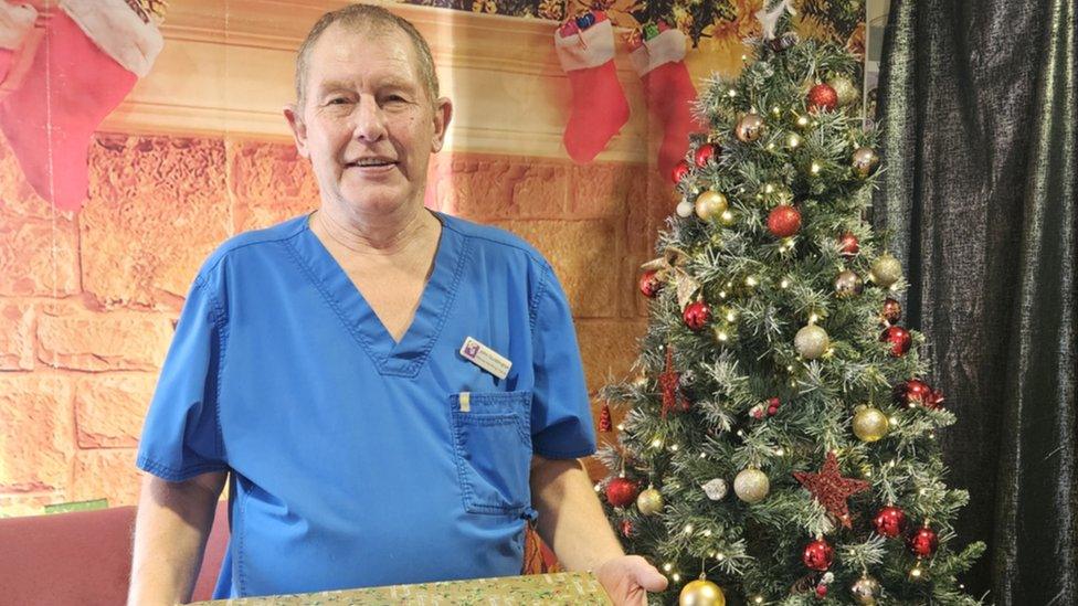 Mr Quiddington standing in front of a Christmas tree in his uniform holding a wrapped present