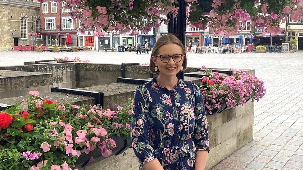 Conservative councillor, Eleanor Wills stood under a hanging basket display of pink flowers