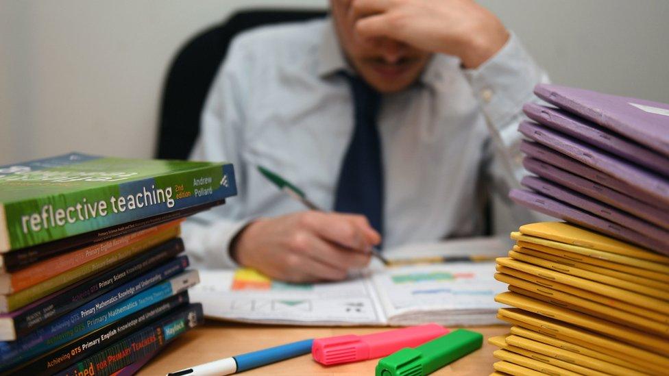 A male teacher leaning his head on his hand whilst surrounded by books