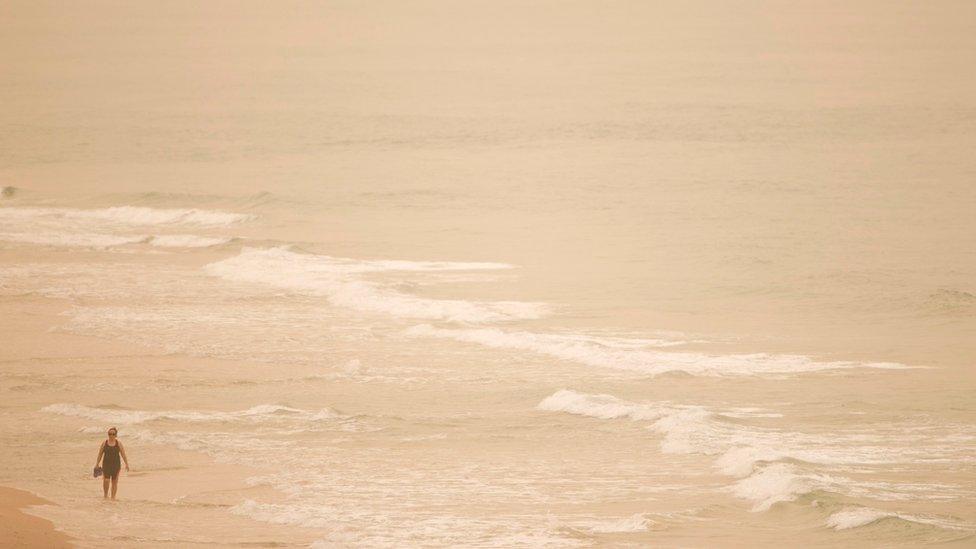 A woman walks on the beach as haze and sand cover the Mediterranean Sea off Beit Yanai, Israel, Tuesday, Sept. 8, 2015