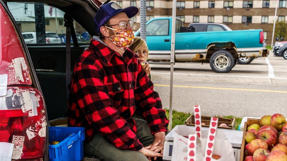 A farmer and his son selling apples from the back of a car