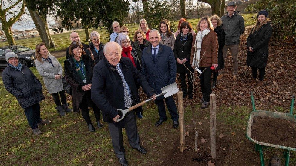 Carl Les planting a tree, surrounded by a crowd