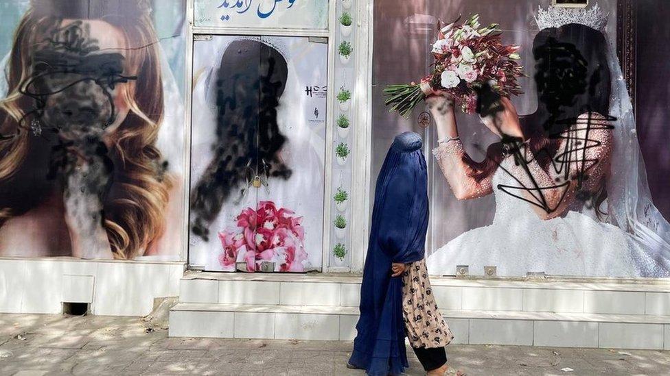 A woman in a burkha walks past a shop where posters of models are covered over