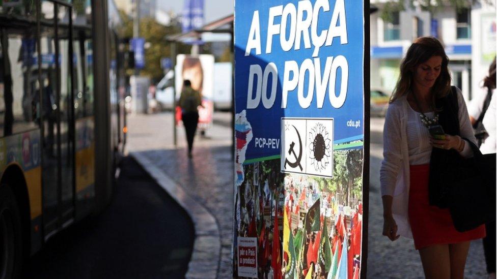 People pass by an election poster of the Portuguese Communist Party and Green Party coalition, in Lisbon Monday, September 2015