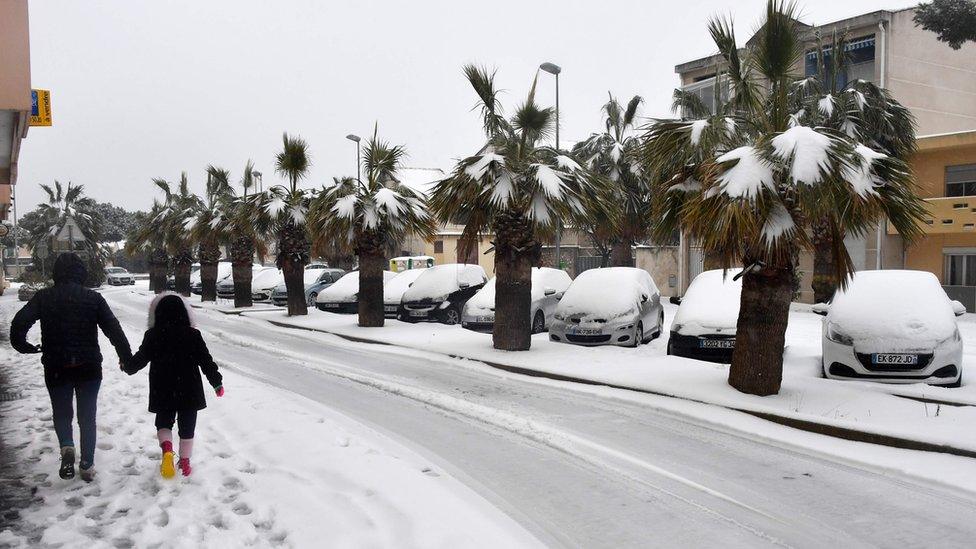 A woman walks with a child down a snow-covered road in Palavas-les-Flots, in the south of France, on February 28, 2018. Europe remained on February 28 gripped by a blast of Siberian weather, accounting for at least 24 deaths and carpeting palm-lined Mediterranean beaches in snow.